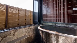 A stone wall with a hot spring, a wooden fence, and a black door. - Ryokan Nagomitsuki (Beppu)
