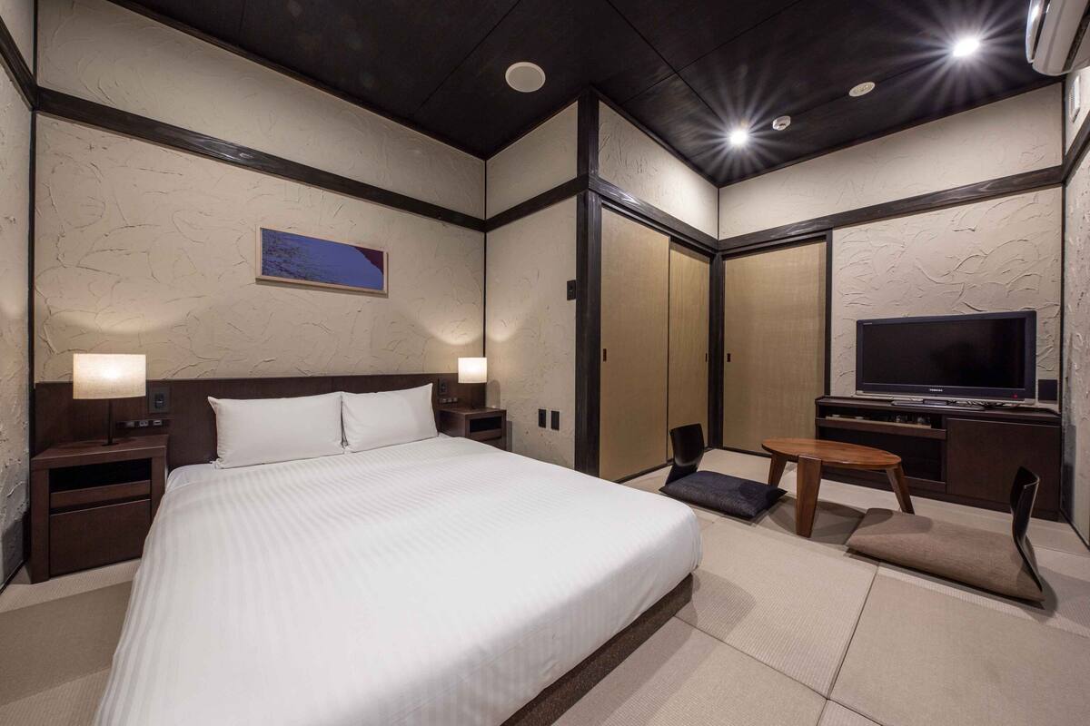 A hotel room with a large bed, a TV, a small table, and a chair.