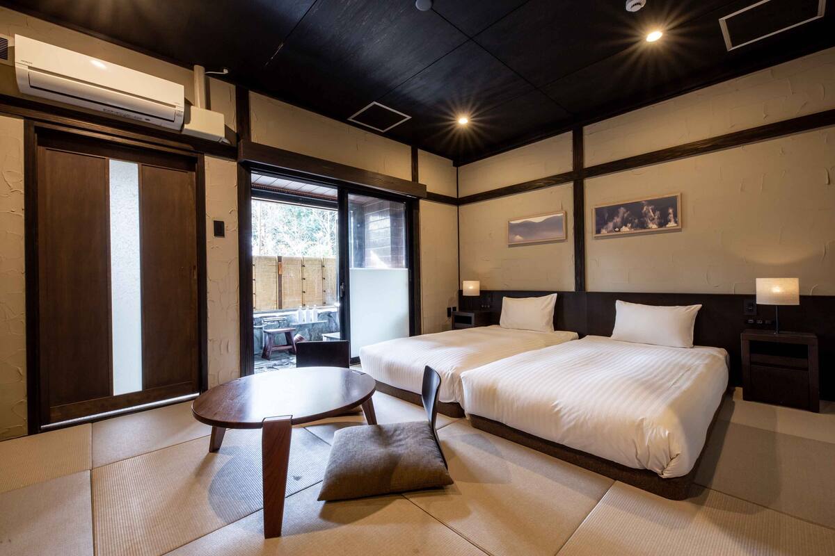 A hotel room with two beds, a dining table, and a view of the outside.