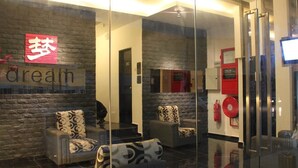 A modern lobby with a stone wall and a glass partition. There are two sofas with patterned cushions, a fire extinguisher, and a television screen. - Dream Hotel (Klang)