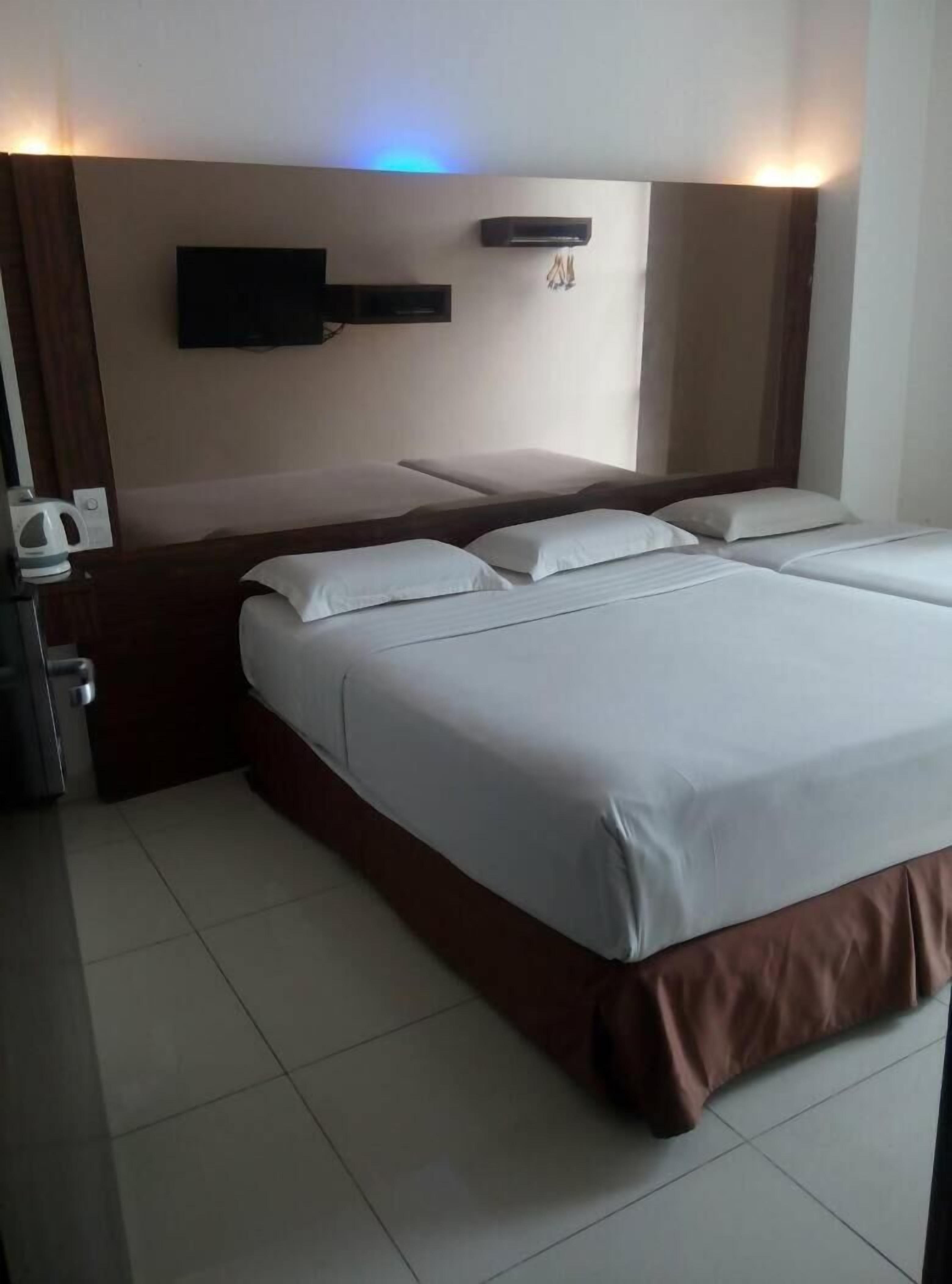A hotel room with a large bed, a flat-screen TV mounted on the wall, and a bedside table with a kettle.
