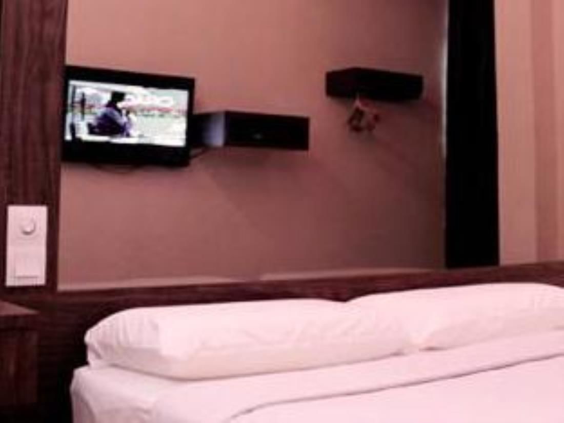 A hotel room with a bed, a television mounted on the wall, and a small shelf.