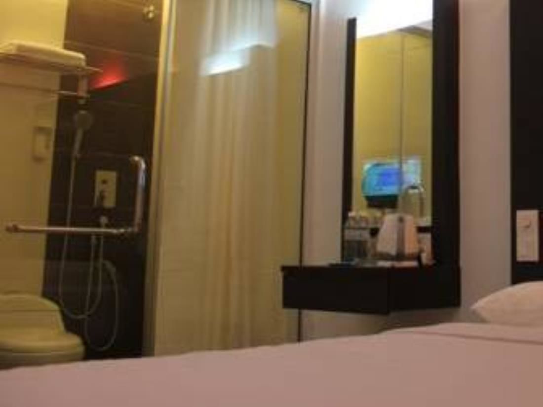 A hotel room with a bed, a bathroom with a shower, and a mirror reflecting part of the room.