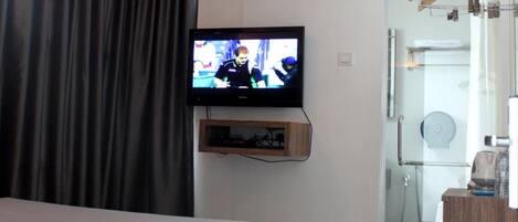 Habitación de hotel moderna con cama, televisión montada en la pared, cabina de ducha de vidrio y cómoda de madera.