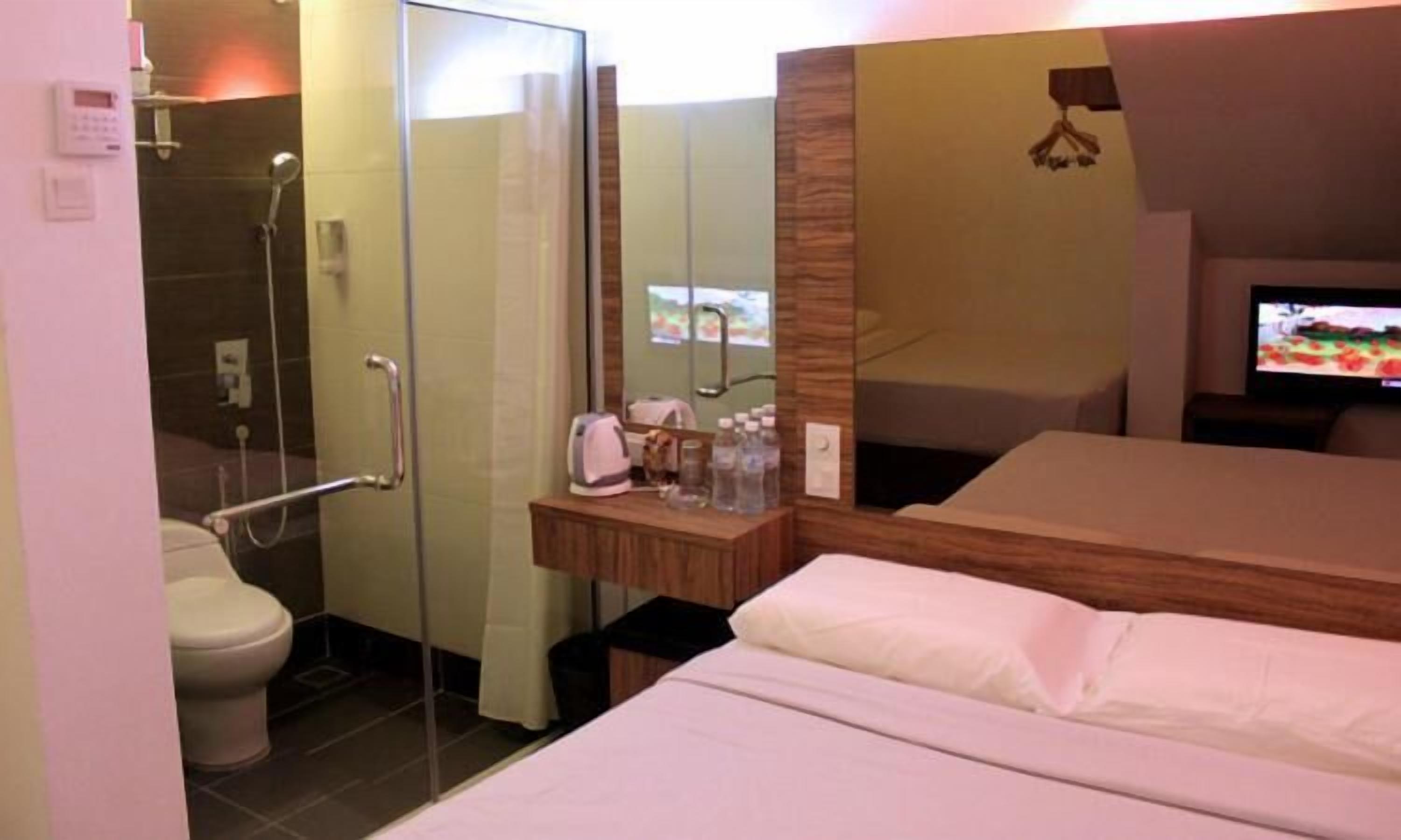Ein Hotelzimmer mit Dusche, WC, Nachttisch mit Pflegeprodukten, einem Bett und einem Fernseher.