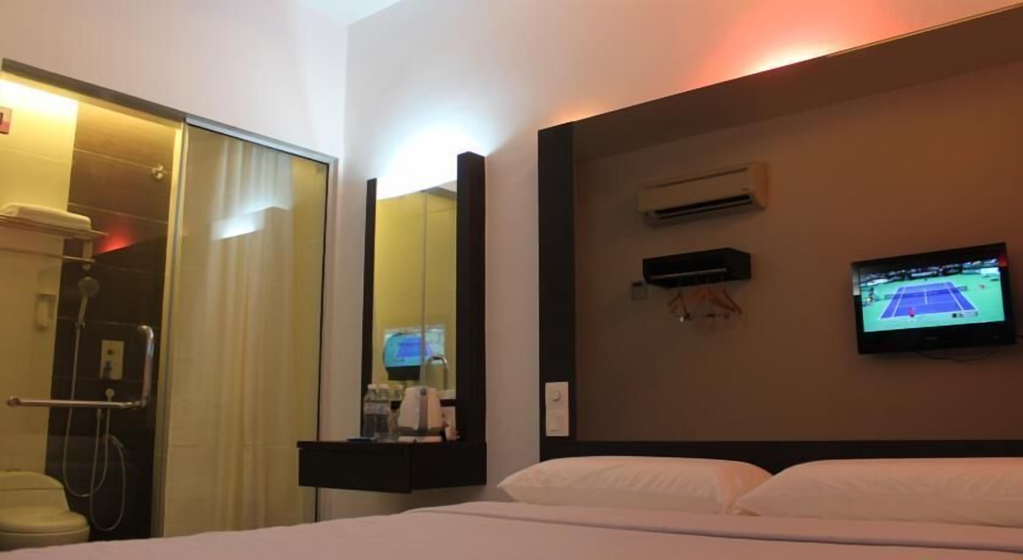 Ein Hotelzimmer mit Bett, Wandfernseher, Duschbereich und Spiegel.