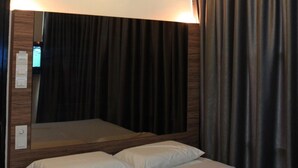 A hotel room with a bed, a ceiling light, a mirror, and dark curtains. - Dream Hotel (Klang)