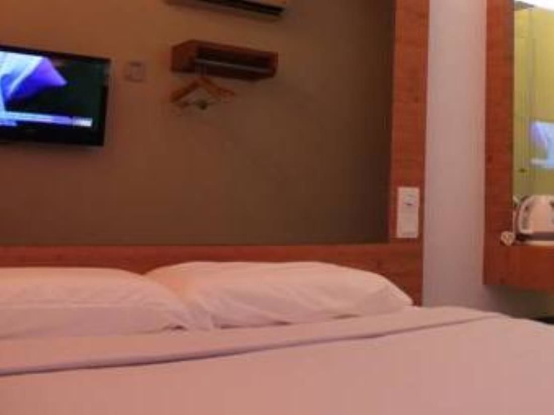 Une chambre d’hôtel avec un lit, un téléviseur fixé au mur et une petite étagère en bois.