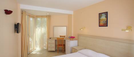 A hotel room with a bed, a desk, a chair, a small refrigerator, a telephone, and a painting on the wall.