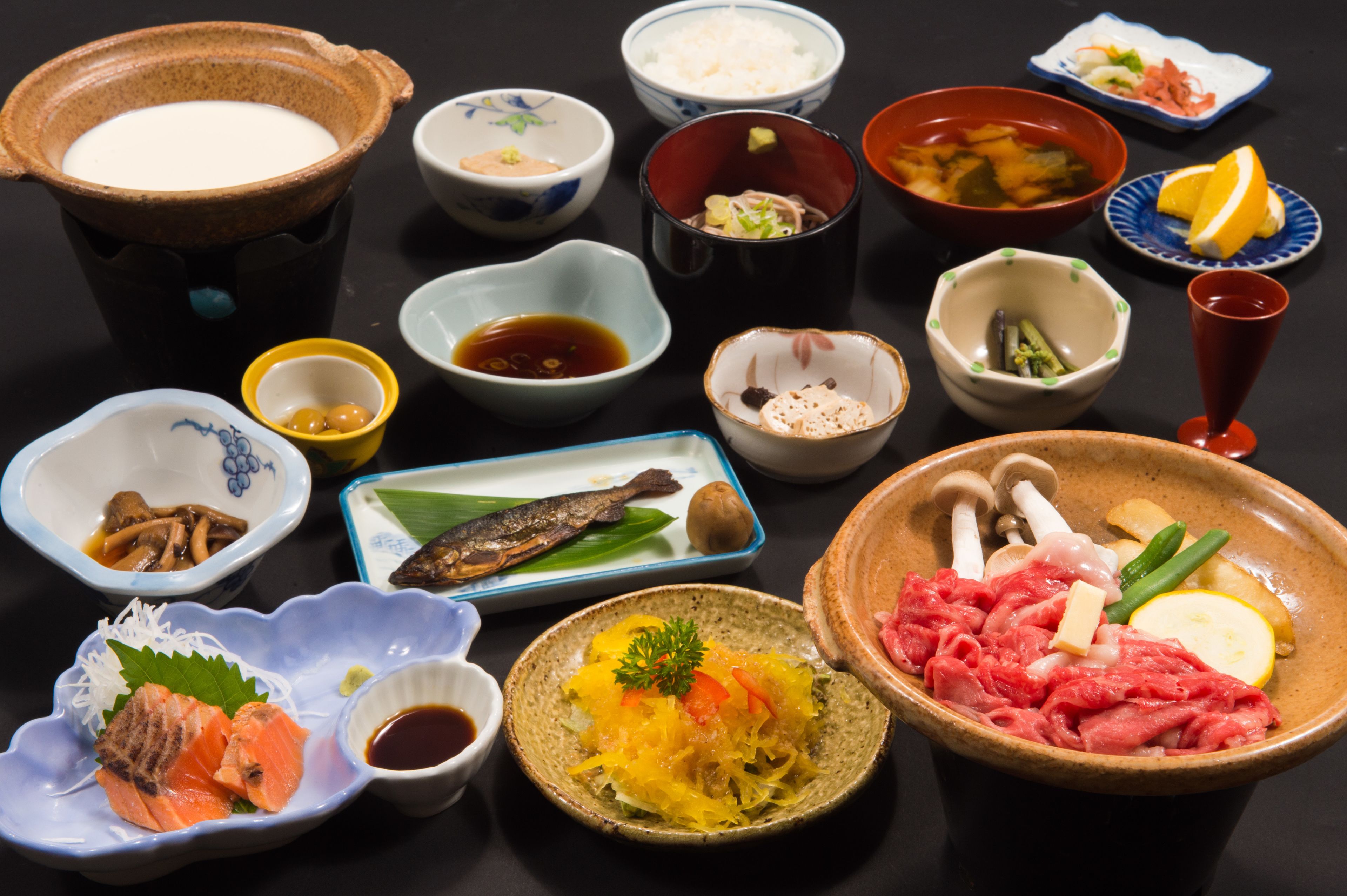 A variety of dishes including sushi, sashimi, and other Japanese cuisine, arranged on a table.