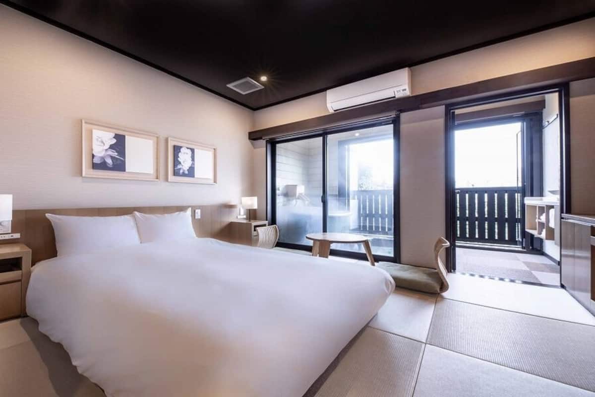 Habitación de hotel con una cama grande, mesitas de noche, una pequeña mesa y un balcón con vistas.