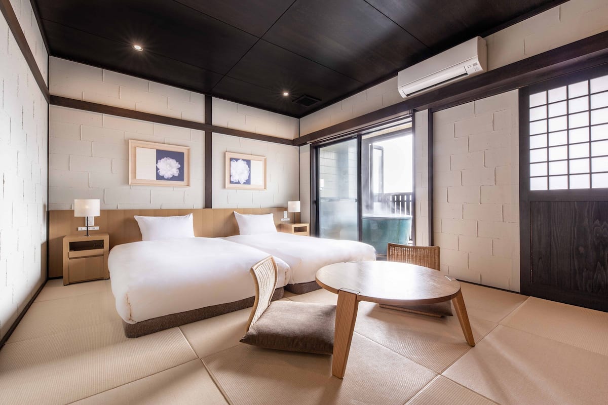 A hotel room with a large bed, a small table, and a view of the outside through a window.