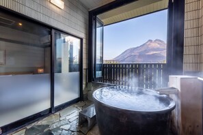 A hot tub with steam, a stone floor, a wooden deck, and a view of a mountain through a window. - Ryokan Kirara (Yufu)