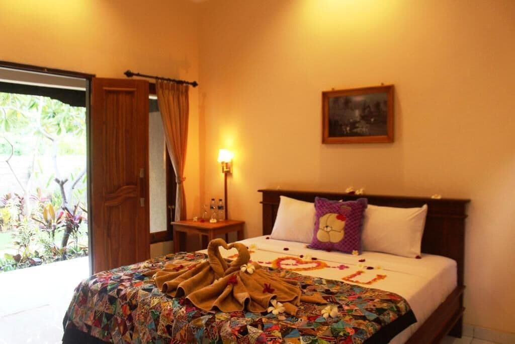 Habitación de hotel con cama, mesita de noche, lámpara, puerta y ventana.