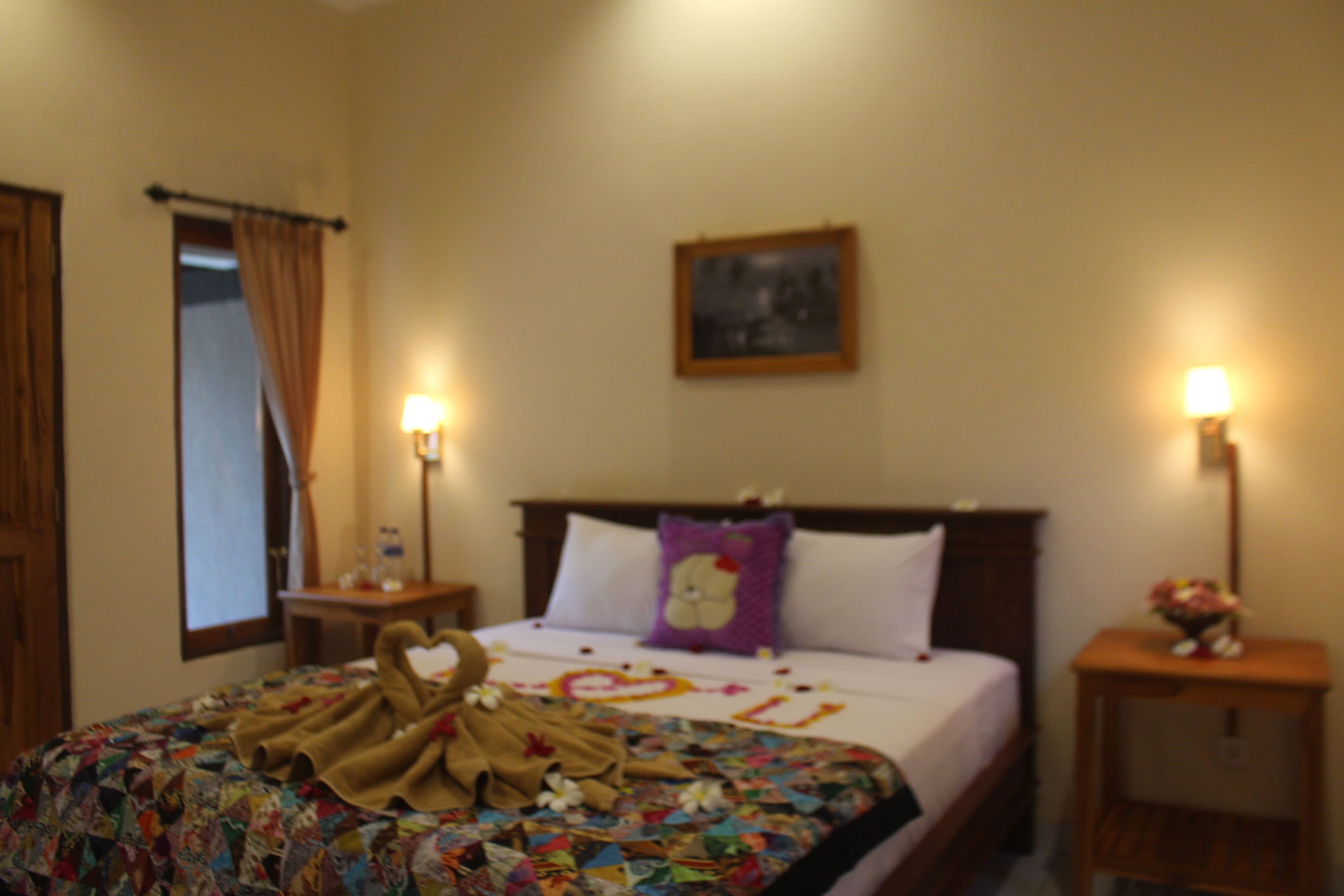 Habitación de hotel con cama, dos mesitas de noche, un ventanal con cortinas y un cuadro colgado en la pared.