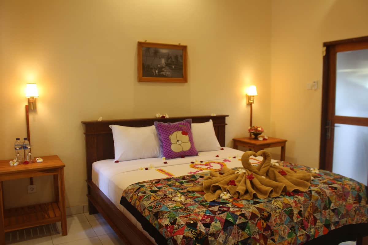 Une chambre d’hôtel avec un lit, deux tables de chevet, une petite table, un tableau encadré au mur et une fenêtre.