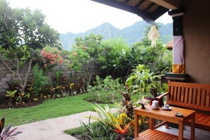 A wooden bench with a table, surrounded by a garden with various plants and a stone wall. - Pande Guest House Pemuteran (Pemuteran)