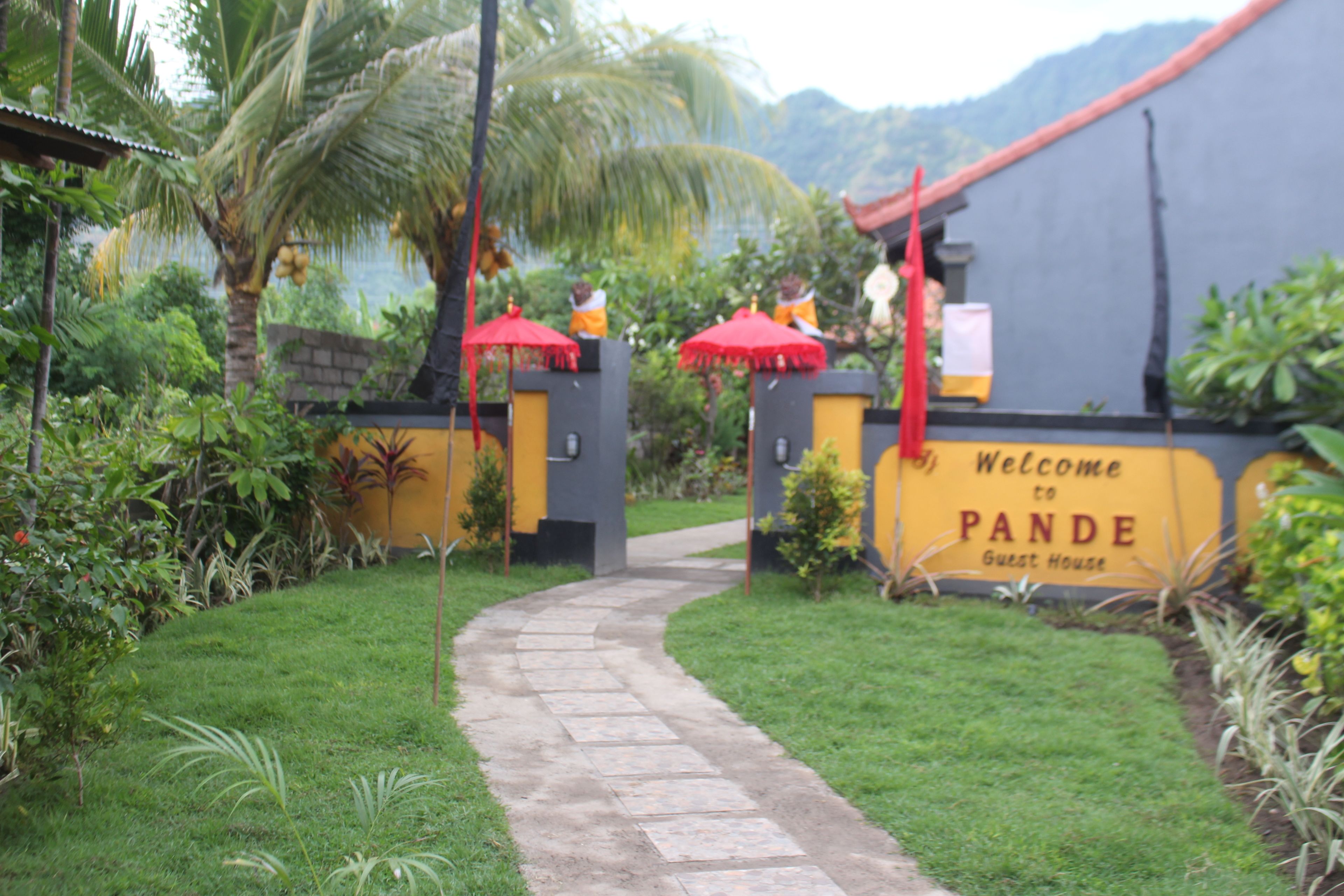 A pathway leading to a building with a sign reading "Welcome to Pande Guest House."