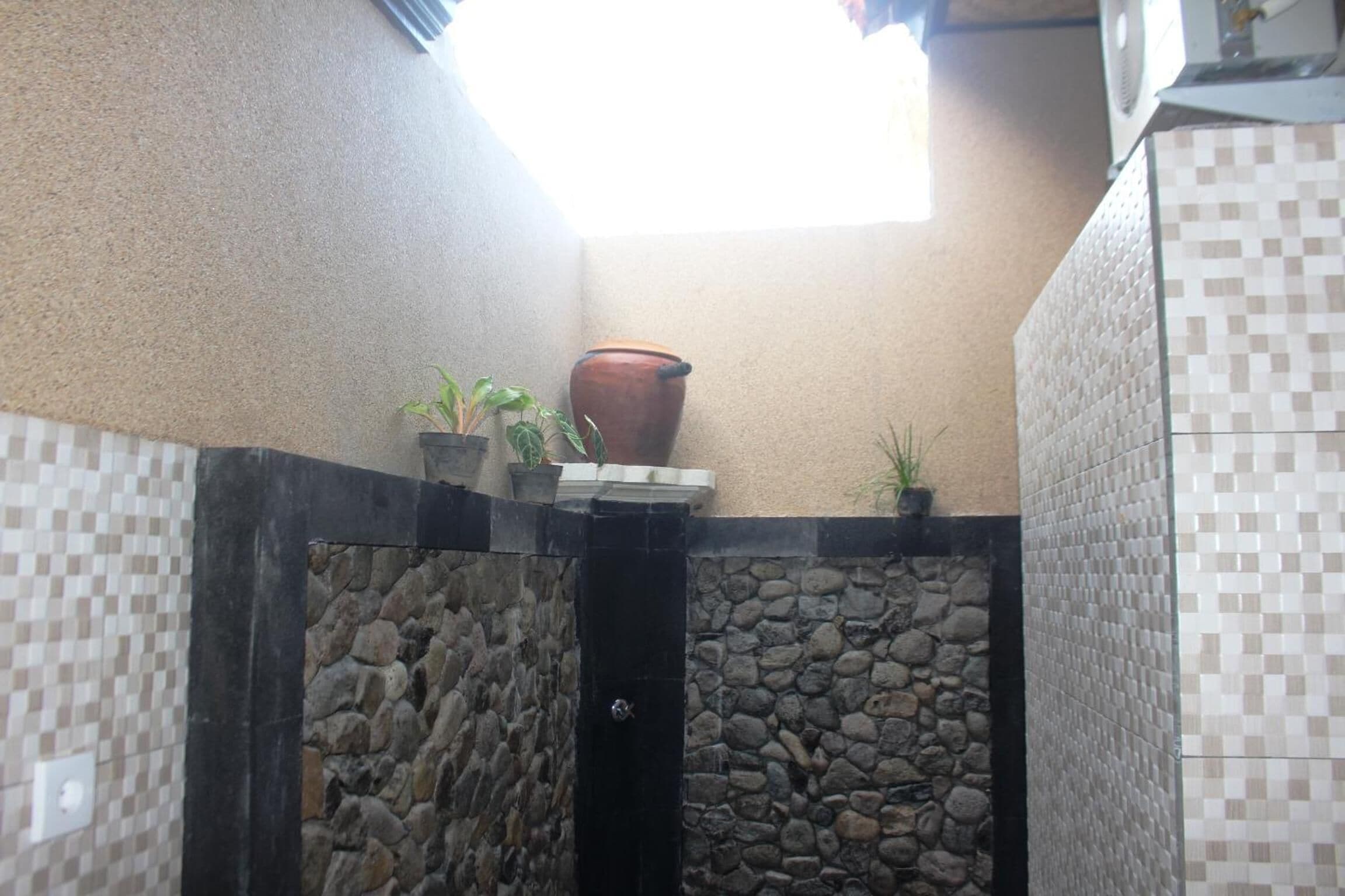 Un baño con pared de piedra, una puerta negra y suelo de baldosas.