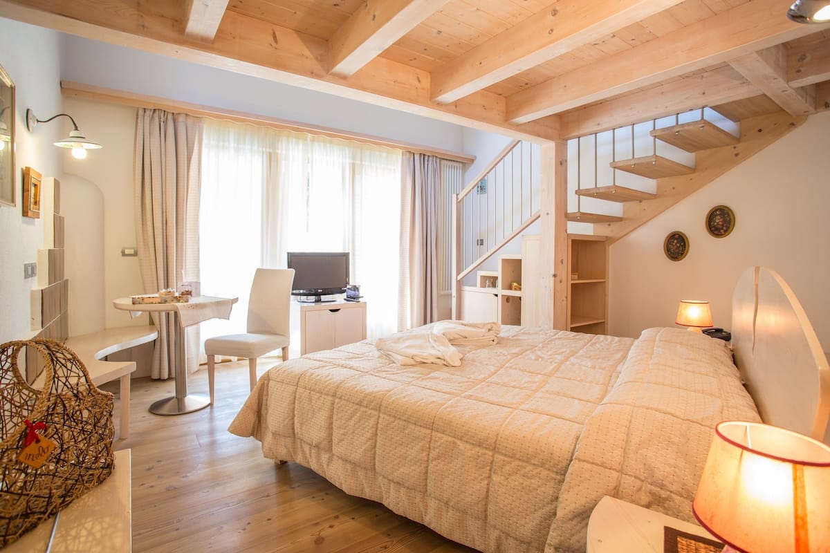 A bedroom with a large bed, a desk with a chair, a television, and a staircase.