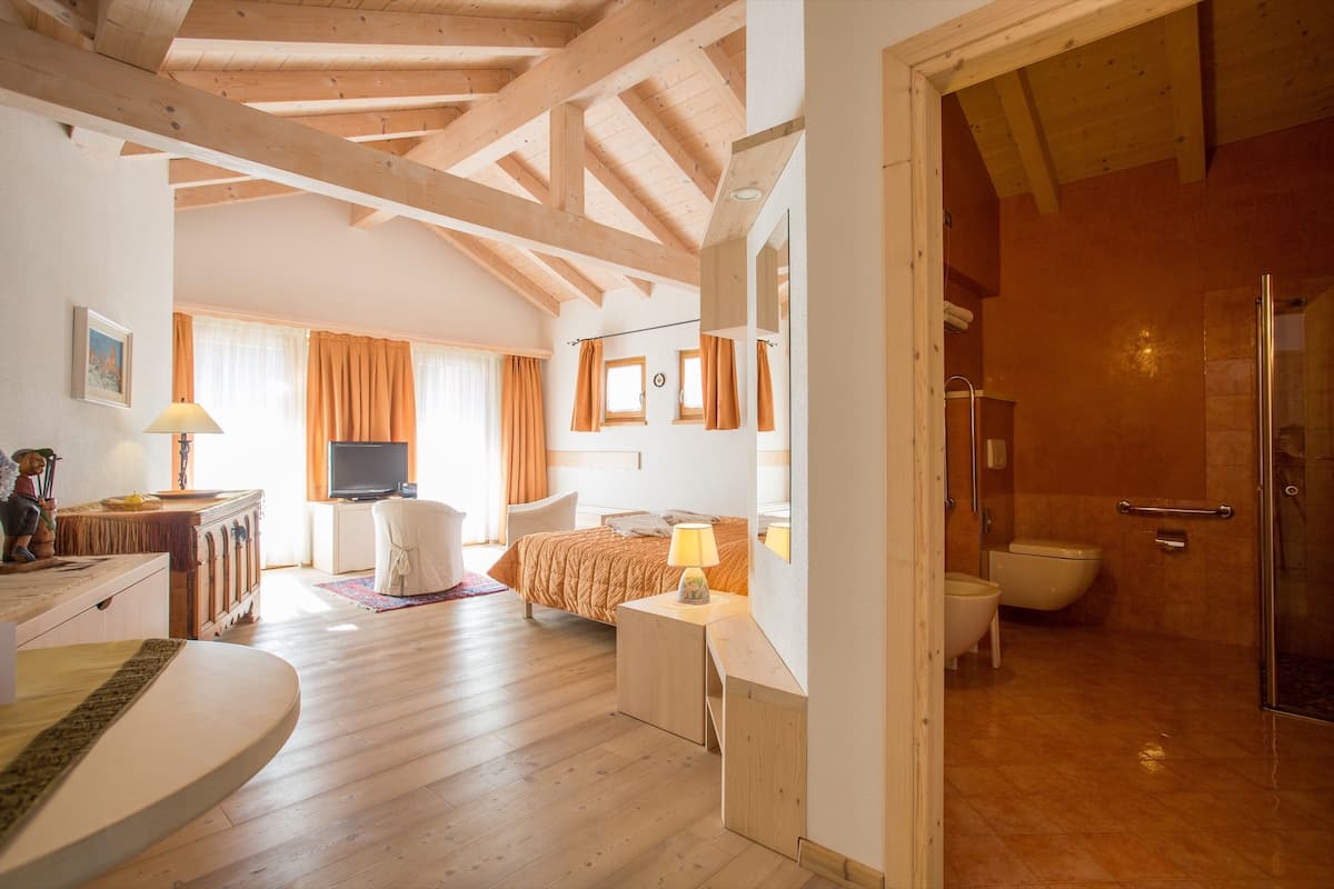 A spacious bedroom with wooden flooring, a large bed, a desk, and a television.