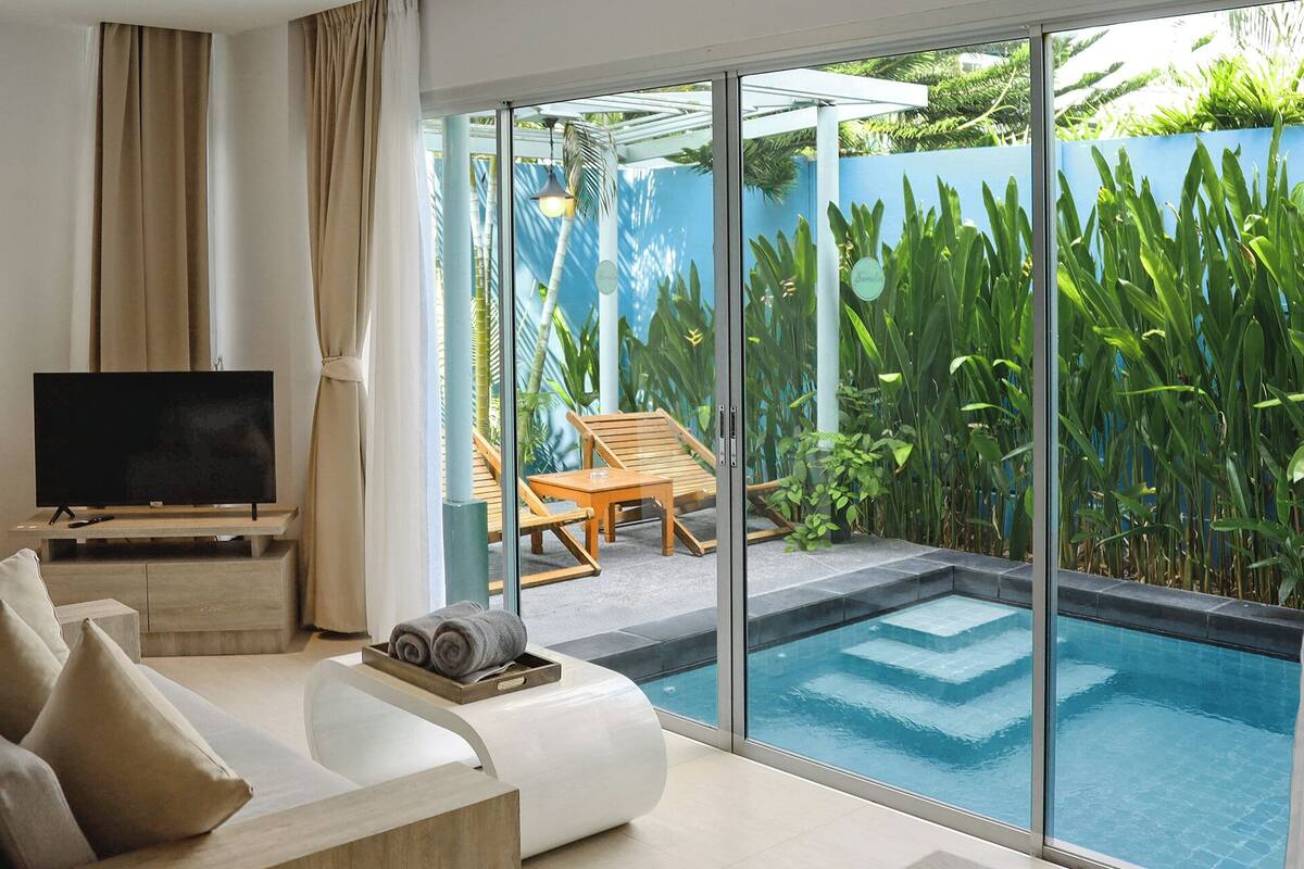 Uma sala de estar moderna com televisão, sofá e vista para uma piscina e vegetação.