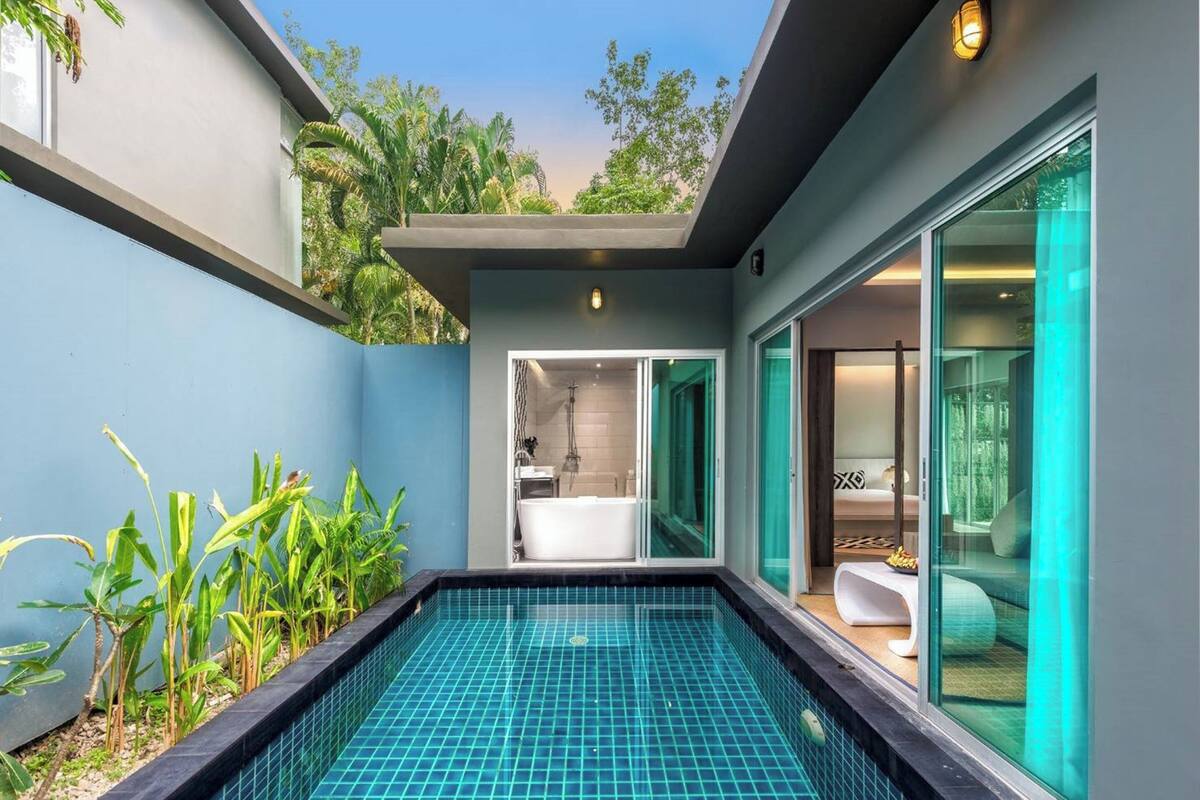 Piscina interior moderna com estrutura de vidro, banheiro visível com banheira e vista para o verde ao redor.