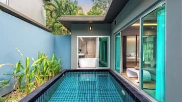 A modern indoor pool with a glass enclosure, a visible bathroom with a bathtub, and a view of the surrounding greenery.