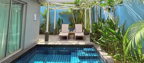 Un petit espace extérieur avec une piscine, deux chaises longues et une pergola, le tout entouré de plantes tropicales.