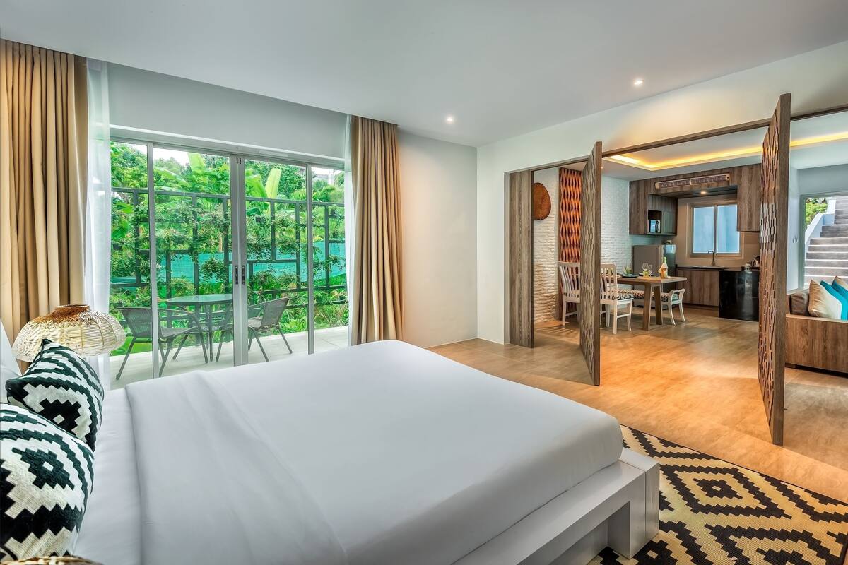 Quarto de hotel com cama, área de refeições e vista para o verde.