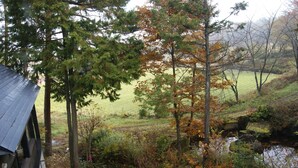 A rustic cabin with a metal roof, surrounded by a forested area with autumn foliage. - Pension Good Luck Takayama (Takayama)