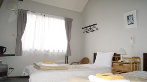 A hotel room with two beds, a window with curtains, a wall-mounted coat rack, a bedside table with a lamp, and a small basket. - Pension Good Luck Takayama (Takayama)