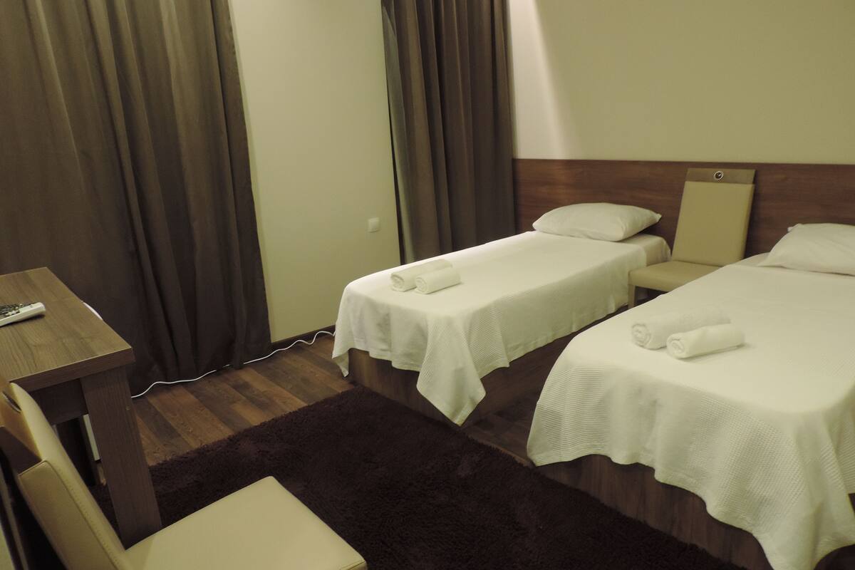 Une chambre d’hôtel avec deux lits simples, une petite table, une chaise et un bureau avec une télécommande.