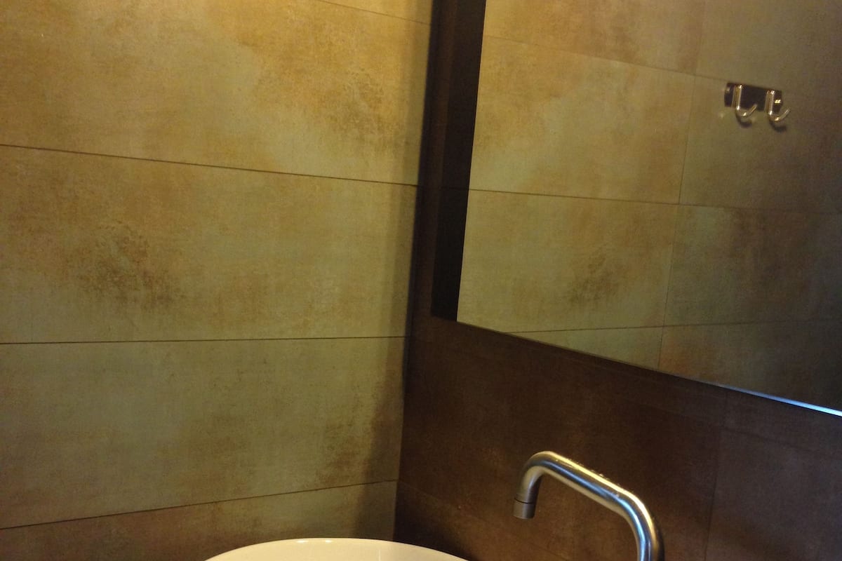 Une salle de bain avec un lavabo blanc, un robinet moderne et un miroir doté d’un cadre métallique.