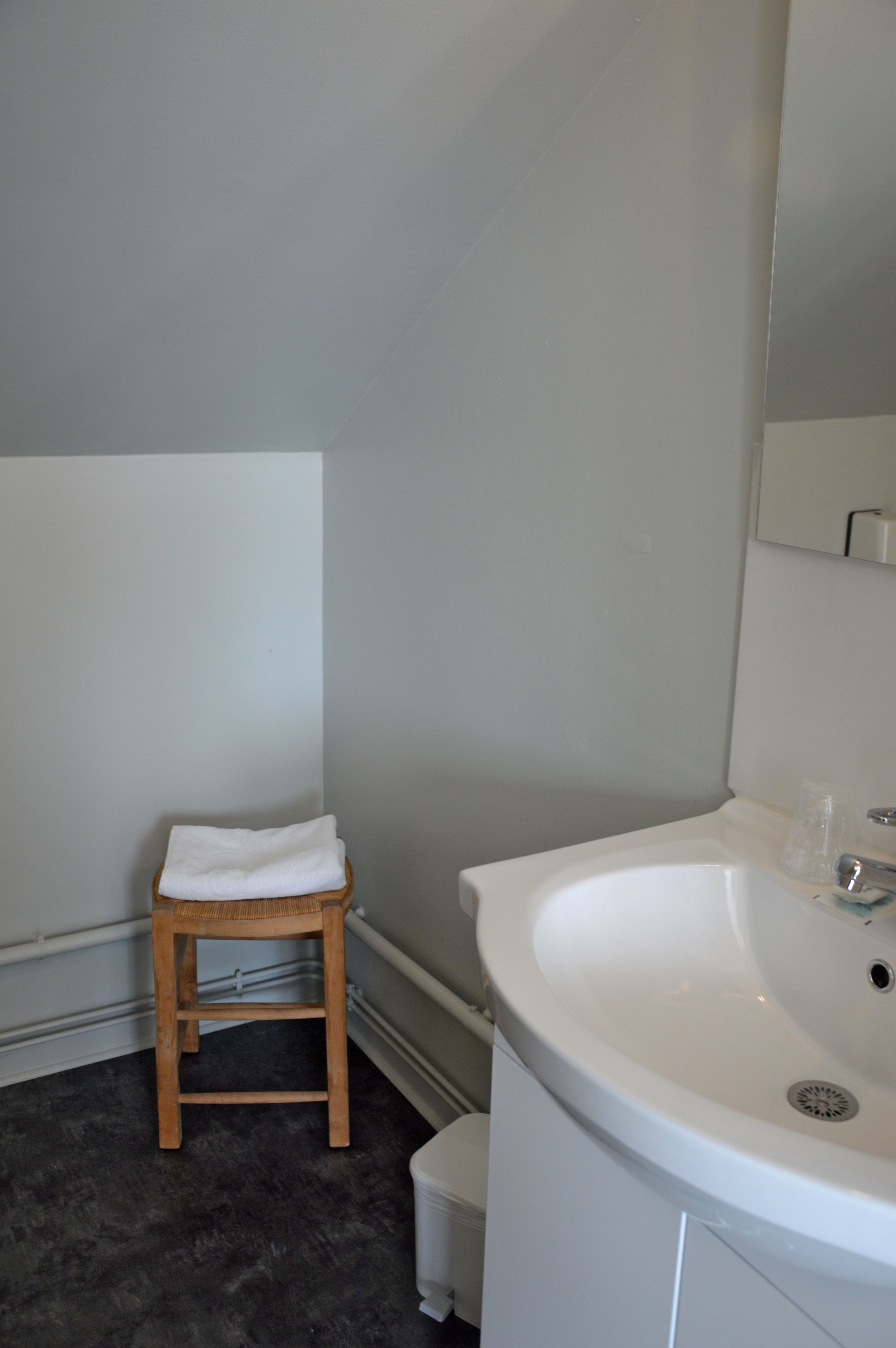 Ein Badezimmer mit einem weißen Waschbecken, einem hölzernen Hocker mit einem weißen Handtuch und einer weißen Toilette.