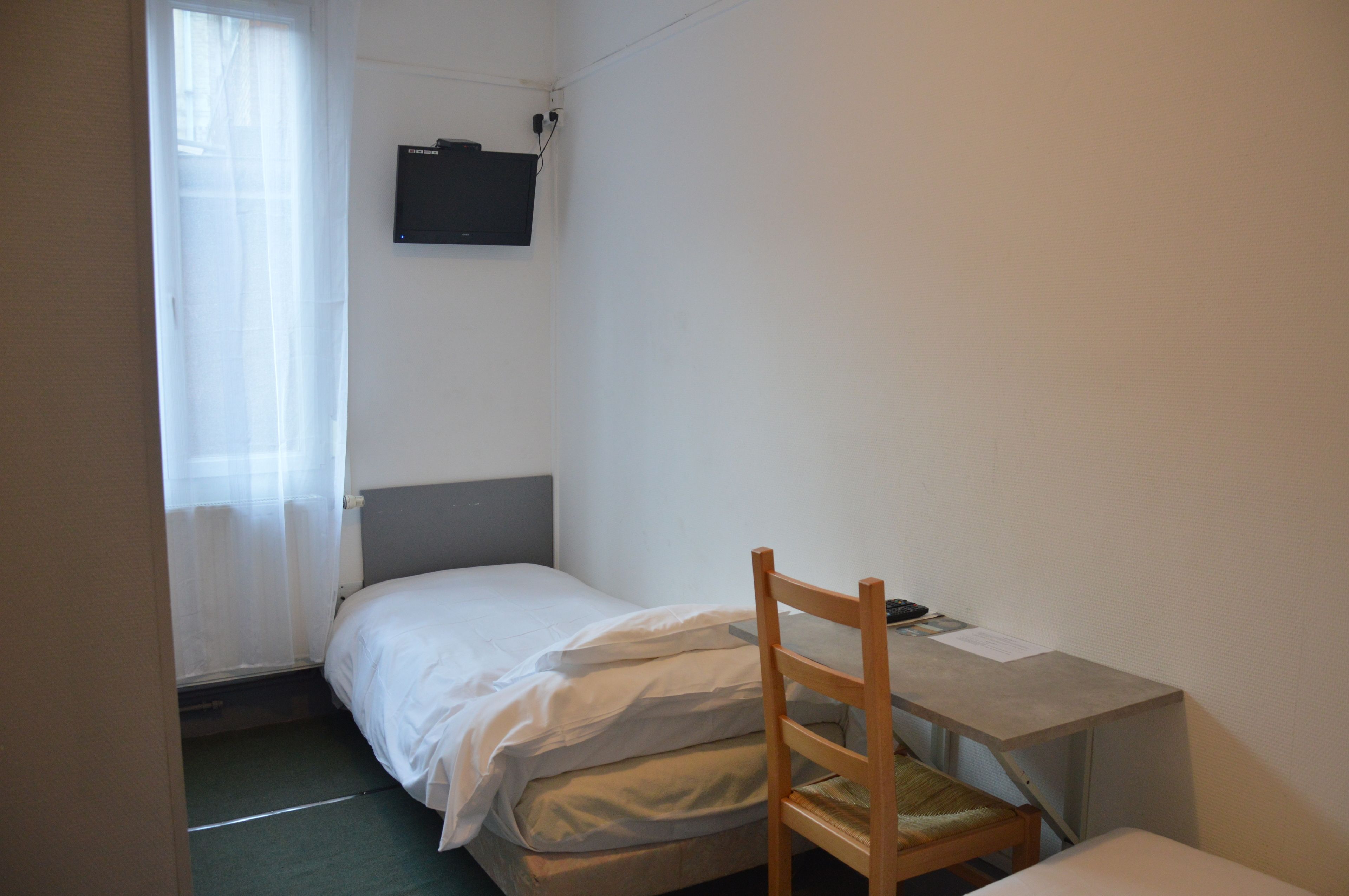A small, sparsely furnished room with a single bed, a desk, and a chair.