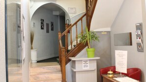 A reception area with a wooden staircase, a reception desk, a potted plant, and a red chair. - Hôtel de Normandie (Amiens)