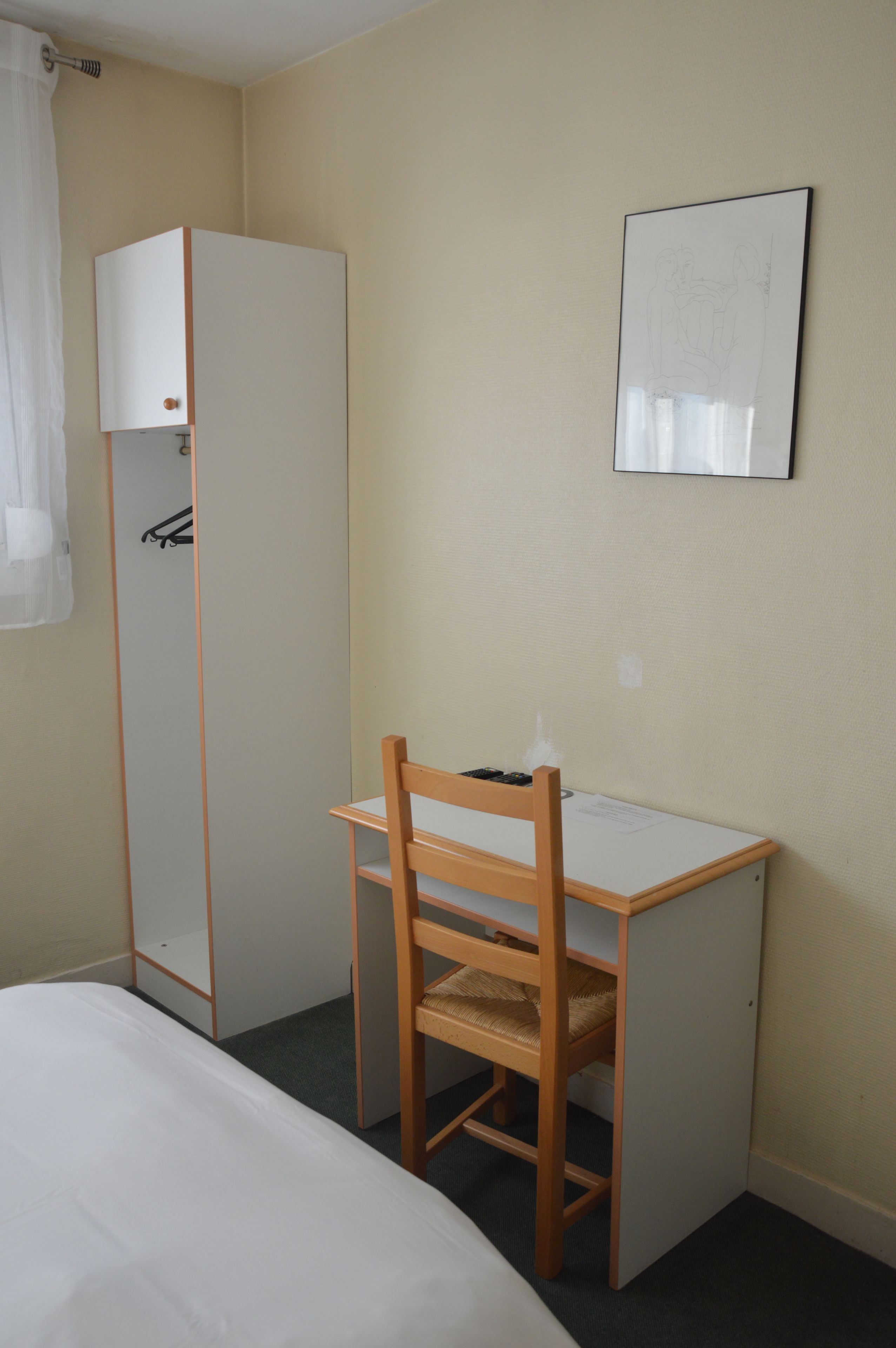Un dormitorio con una cama individual, un escritorio de madera con una silla, un armario y un cuadro en la pared.