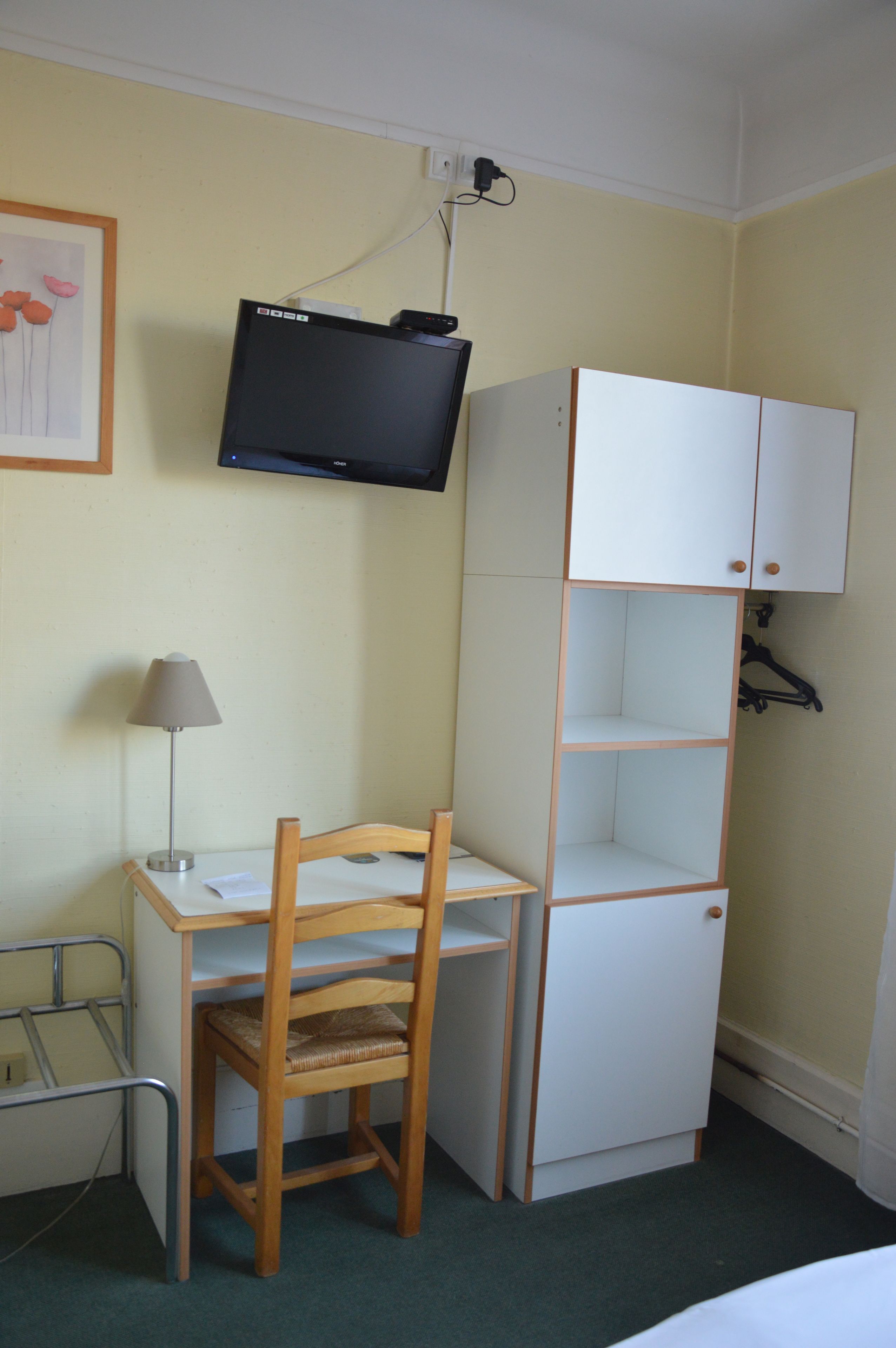 A small room with a desk, chair, television, and a white wardrobe.