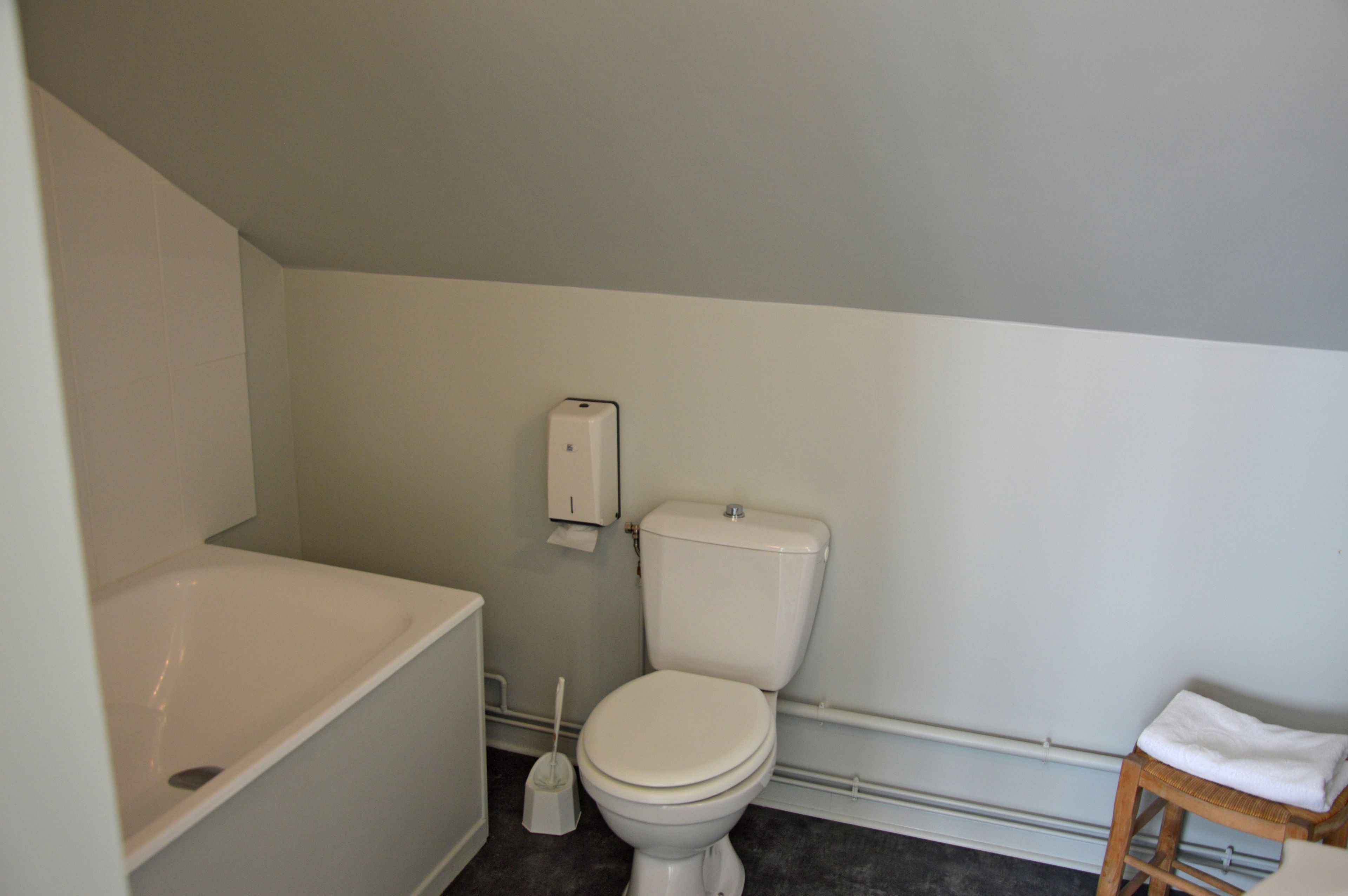 Une salle de bain avec une baignoire, des toilettes et un petit tabouret en bois.