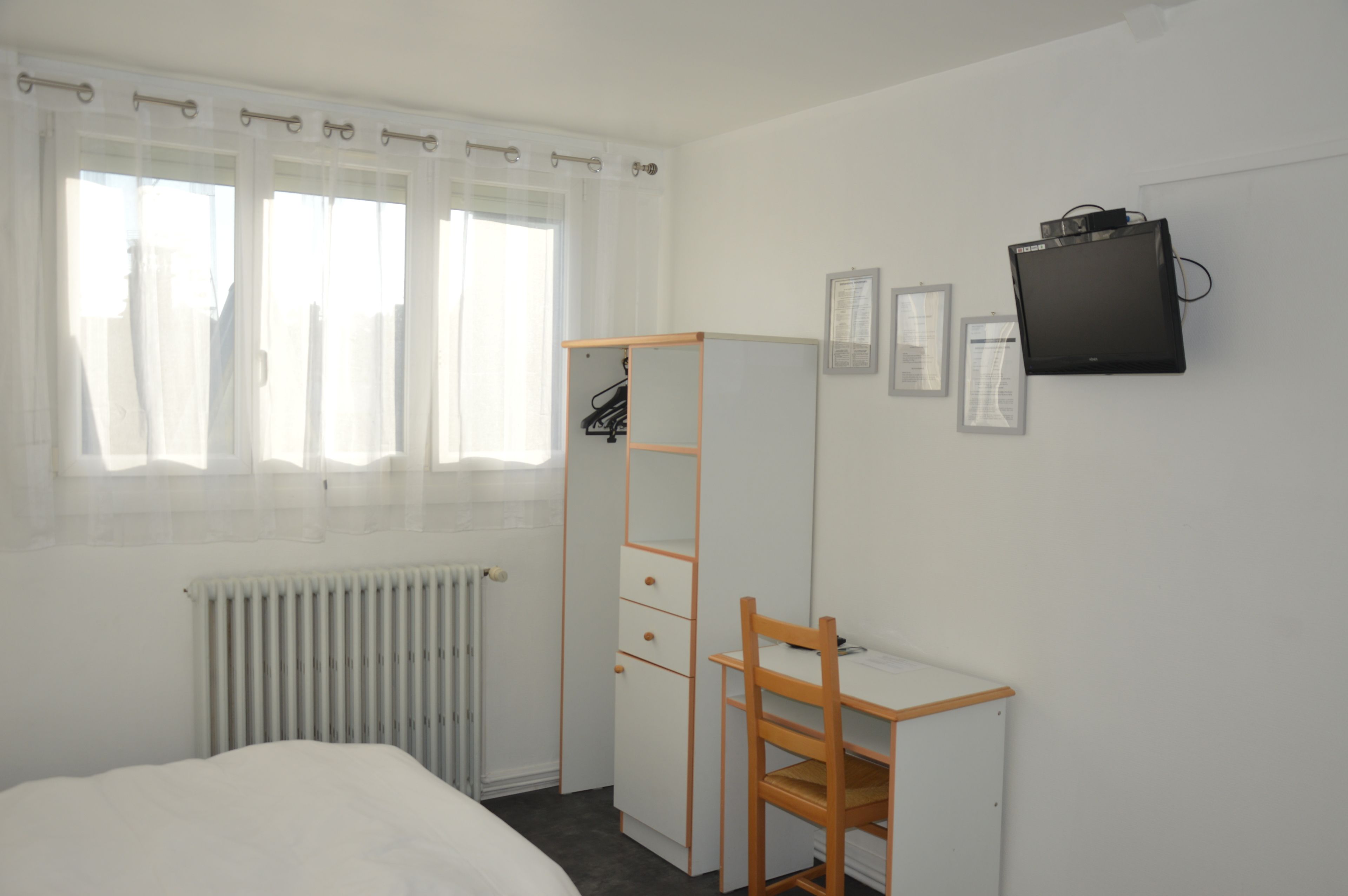 A bedroom with a bed, a desk, a chair, a wardrobe, a radiator, and a TV mounted on the wall.