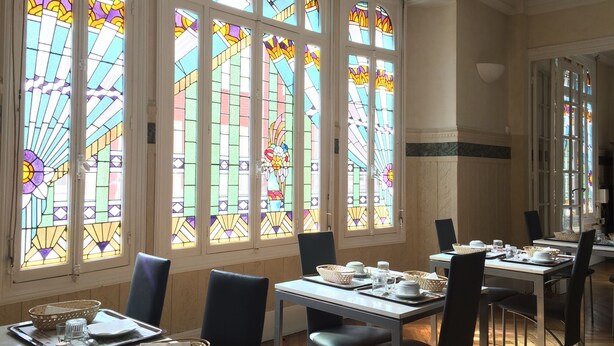 A dining area with large stained glass windows, wooden paneling, and a table set for two. - Hôtel de Normandie (Amiens)