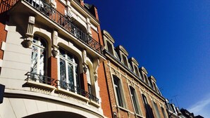 A hotel facade with a prominent arched entrance and a balcony with ornate iron railings. - Hôtel de Normandie (Amiens)