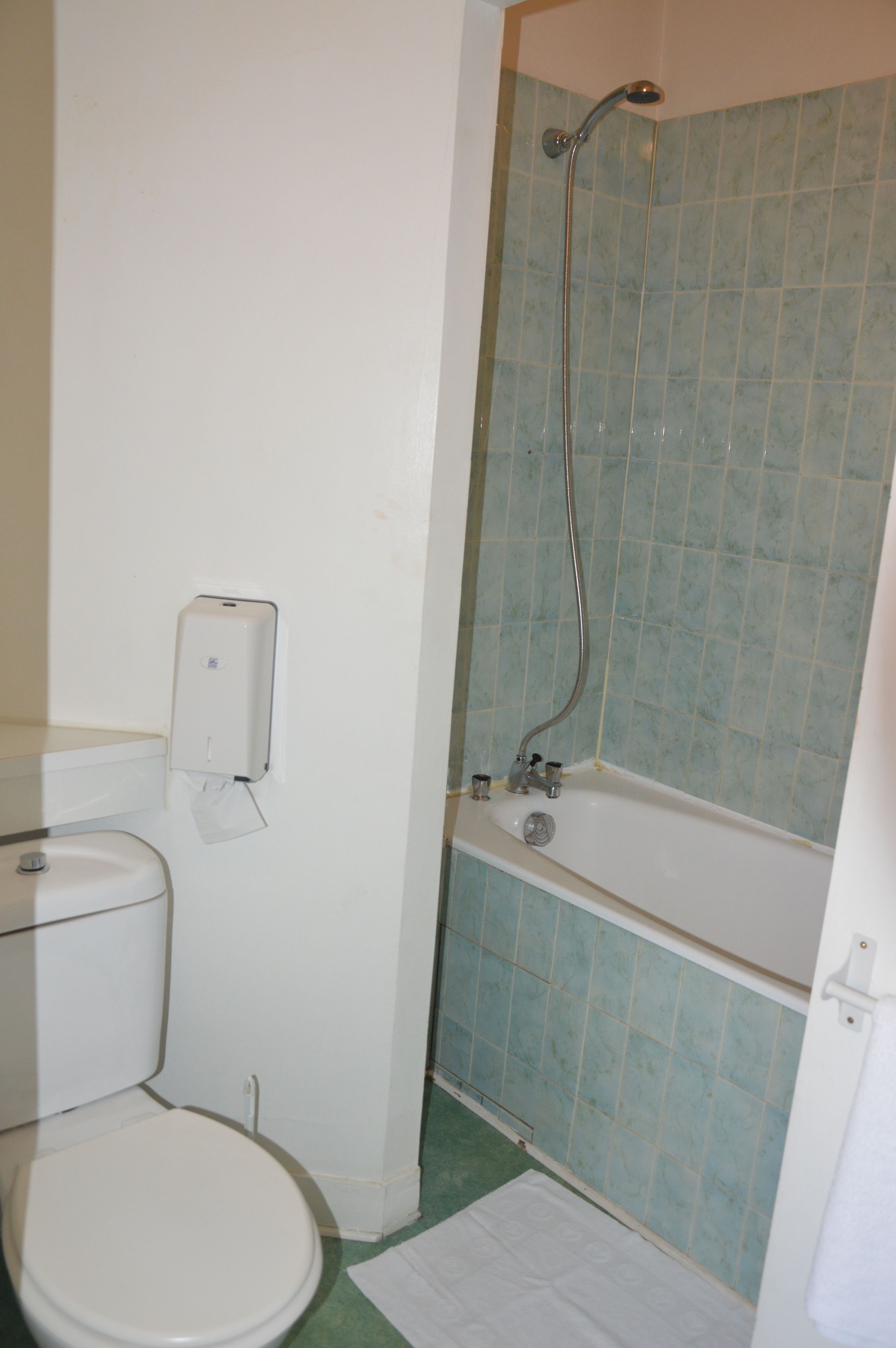 Un baño con inodoro, dispensador de toallas de papel, ducha con cabezal de ducha manual y bañera.