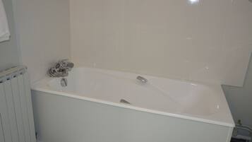 A white bathtub with a showerhead and faucet, a white radiator, and a white tiled wall.