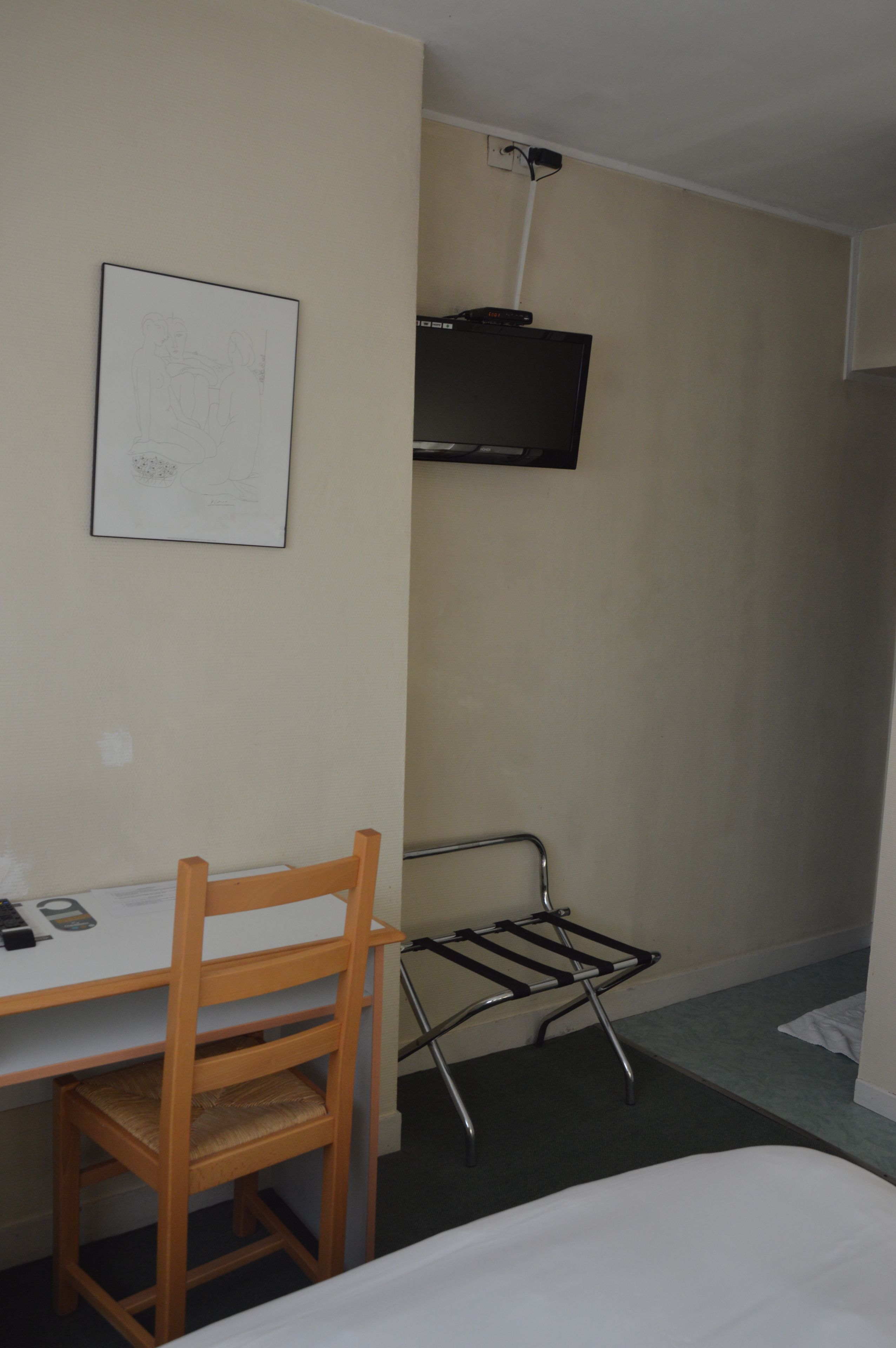 A hotel room with a wooden desk, a chair, a bed, a TV mounted on the wall, and a wall-mounted towel rack.
