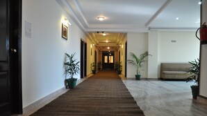Un pasillo de hotel con piso alfombrado, plantas en macetas, un sofá y una puerta a la izquierda.
