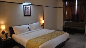 Una habitación de hotel con una cama grande, dos lámparas de noche, una mesita de noche, un sofá y una ventana con cortinas.
