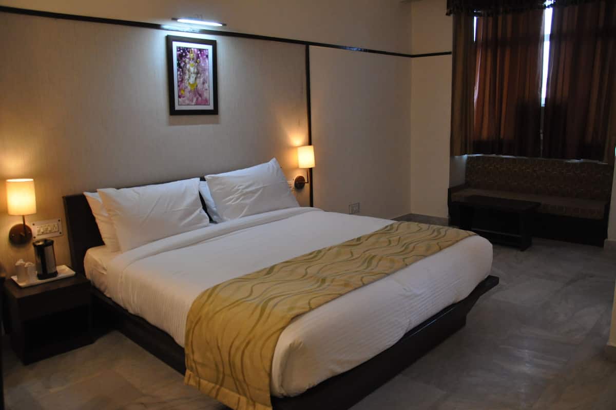 Una habitación de hotel con una cama grande, dos lámparas de noche, una mesita de noche, un sofá y una ventana con cortinas.