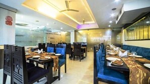 Un restaurante con mesas altas y asientos tipo banca acolchados en azul, que presenta un diseño de techo moderno con iluminación empotrada.